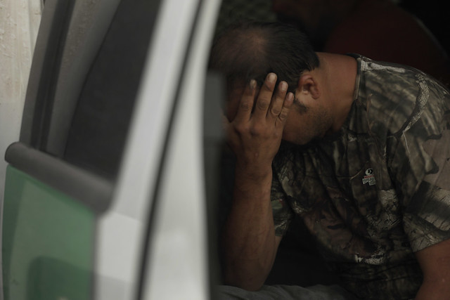 An apprehended migrant sits in a truck with his hands in his face