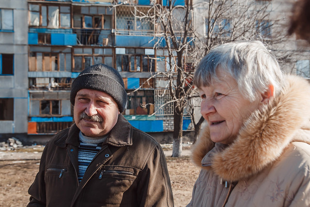 An older man and woman stand in front of an apartment building