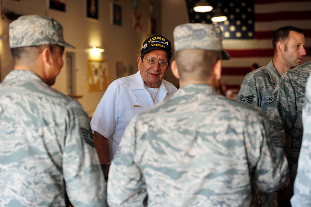 Two men in military attire stand with a veteran