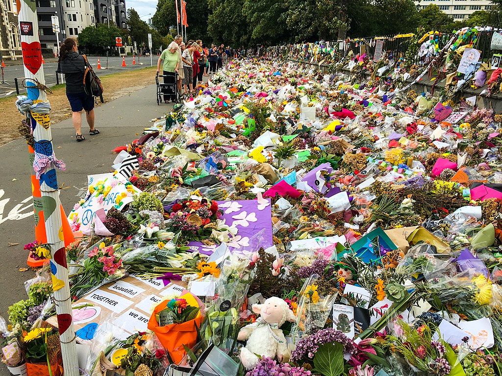 People pass by flowers laying on a street